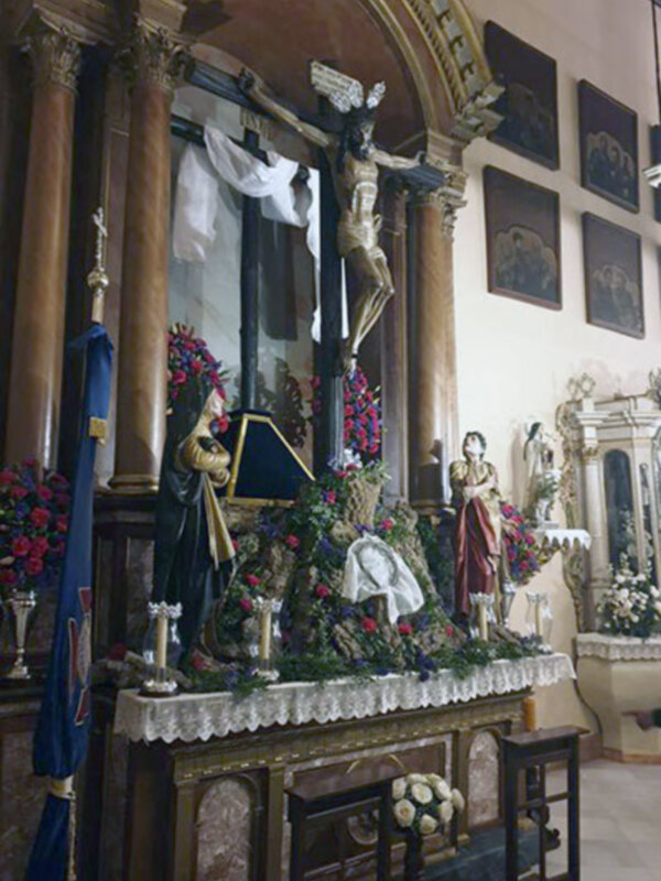 Altar con estatuas religiosas, flores y velas encendidas.