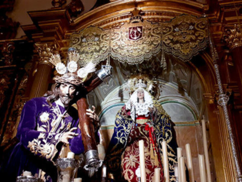 Estas imágenes muestran una escena religiosa dentro de una iglesia, con dos figuras importantes vestidas en trajes tradicionales y adornadas con joyas. La figura principal está vestida de azul y lleva un sombrero, mientras que la otra figura está vestida de rojo con una corona. Ambas figuras están en un altar ricamente decorado, con detalles dorados y una cruz visible. La escena transmite un sentimiento de reverencia y solemnidad típico de la religión católica.