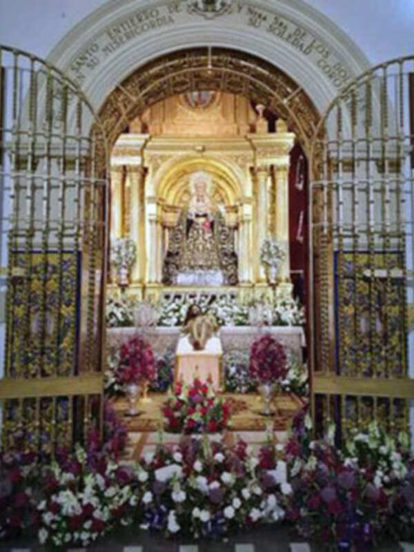 Altar dorado con estatua central, flores y adornos religiosos.