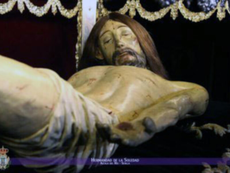 Representación escultórica de Cristo en la cruz, con detalles en la piel y ropa, bajo un arco decorativo.