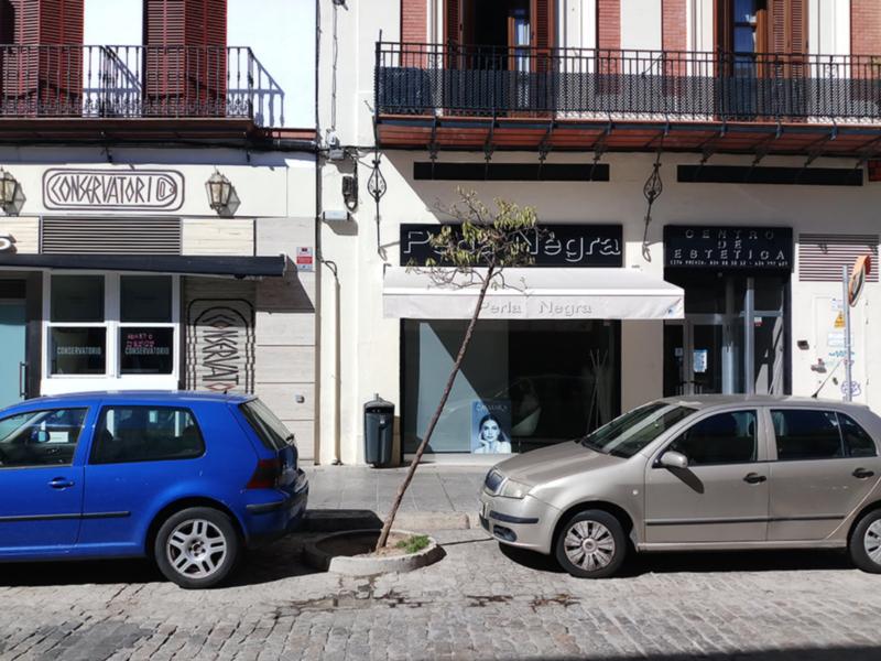 Vista de una calle con tiendas y coches aparcados en un entorno urbano.