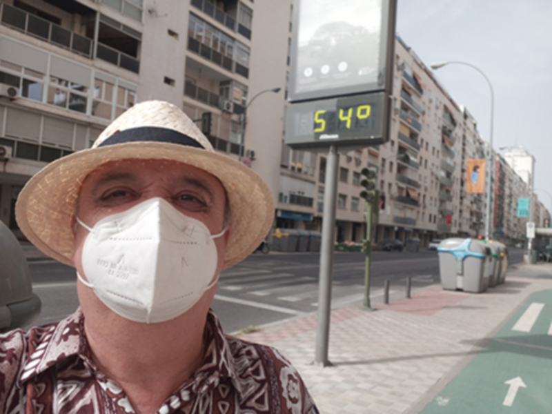 Un hombre con una gorra de paja y una máscara facial blanca. En el fondo, edificios altos con ventanas y una calle con un semáforo que muestra 540.