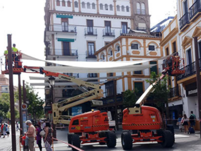Trabajadores en elevadores de altura realizando tareas en una calle con edificios históricos al fondo.
