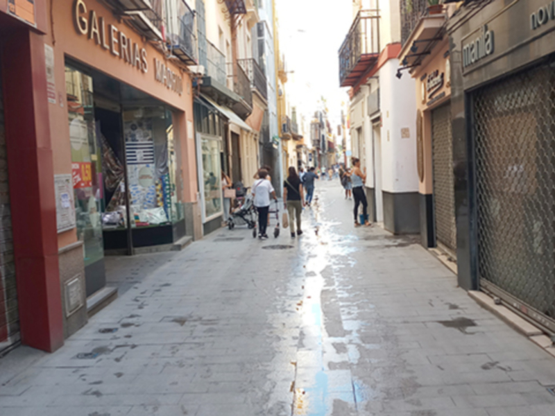 Calles de una ciudad con tiendas y grafitis, gente caminando.