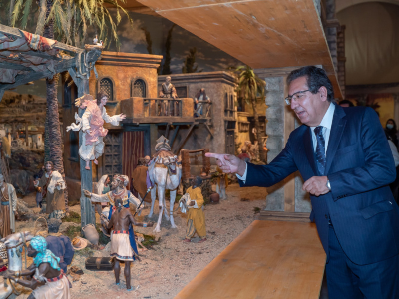 Un hombre en traje señala una escena del Nacimiento de Jesús en un belén, rodeado de figuras y detalles tradicionales.