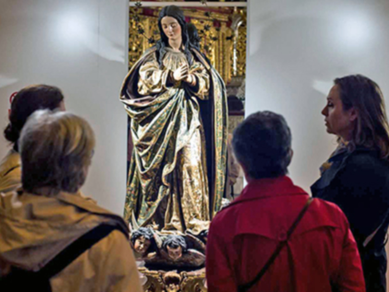 Visitas guiadas a una exposición de arte religioso, enfocándose en una estatua tallada y dorada.