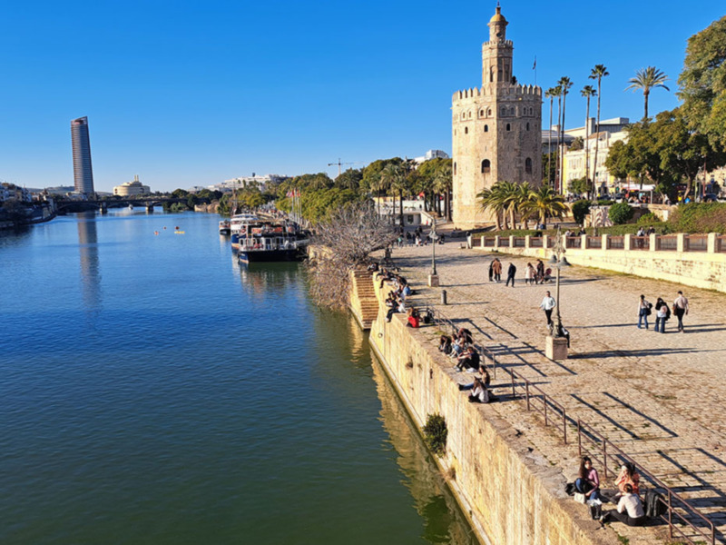Torre del Oro, Sevilla, con turistas disfrutando del paisaje junto al río Guadalquivir.