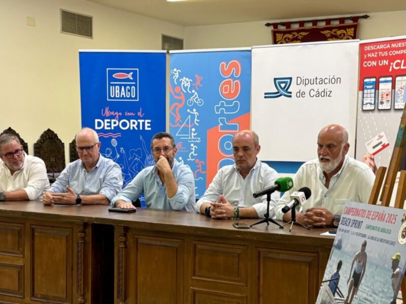 Un grupo de personas se reúnen en una conferencia de prensa, con banners que promocionan el deporte y la Diputación de Cádiz.