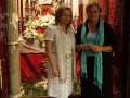 Dos mujeres posan frente a un altar con velas y flores, en un entorno religioso.