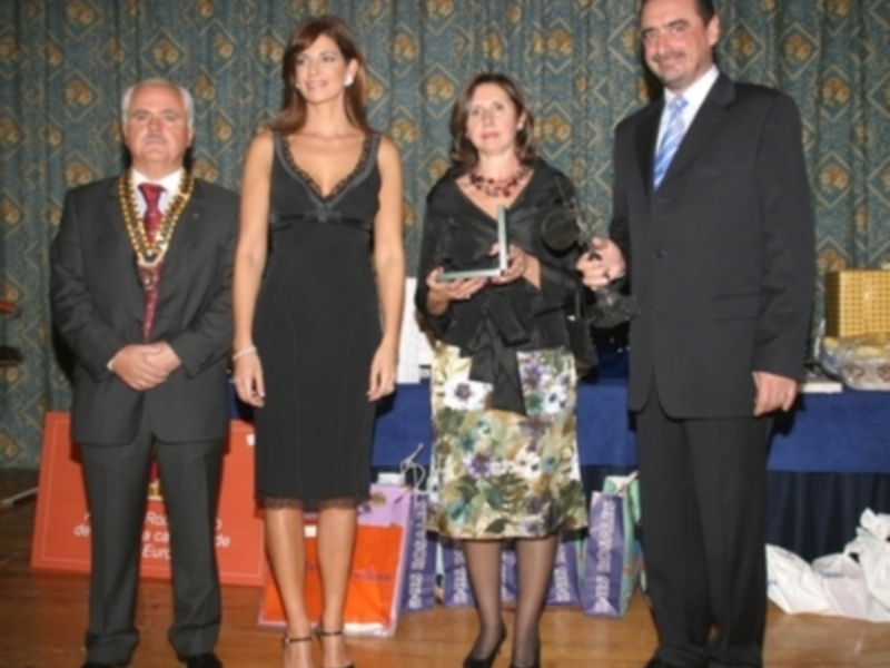 Personas posando en un evento formal, con una mujer en el centro sosteniendo un premio.