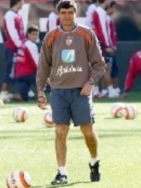 Entrenador de fútbol supervisando un entrenamiento con balones y uniformes deportivos alrededor.