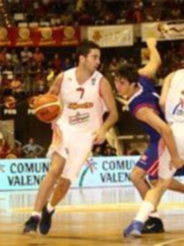 Un jugador de baloncesto en acción, con el número 7 en su camiseta, corre hacia la canasta mientras otros jugadores lo persiguen. La imagen muestra un partido de baloncesto en una cancha con publicidad de "Comil Valencia" y otros anuncios.