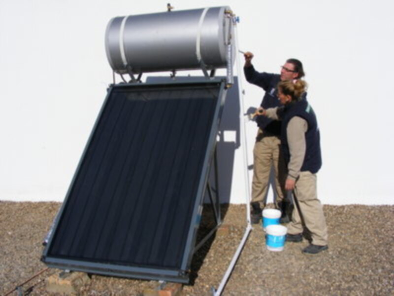 Un equipo de mantenimiento inspecciona un sistema solar térmico, mostrando una cubeta y un tubo de acero.