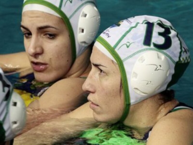 Dos jugadoras de waterpolo en acción, con cascos blancos y verdes.
