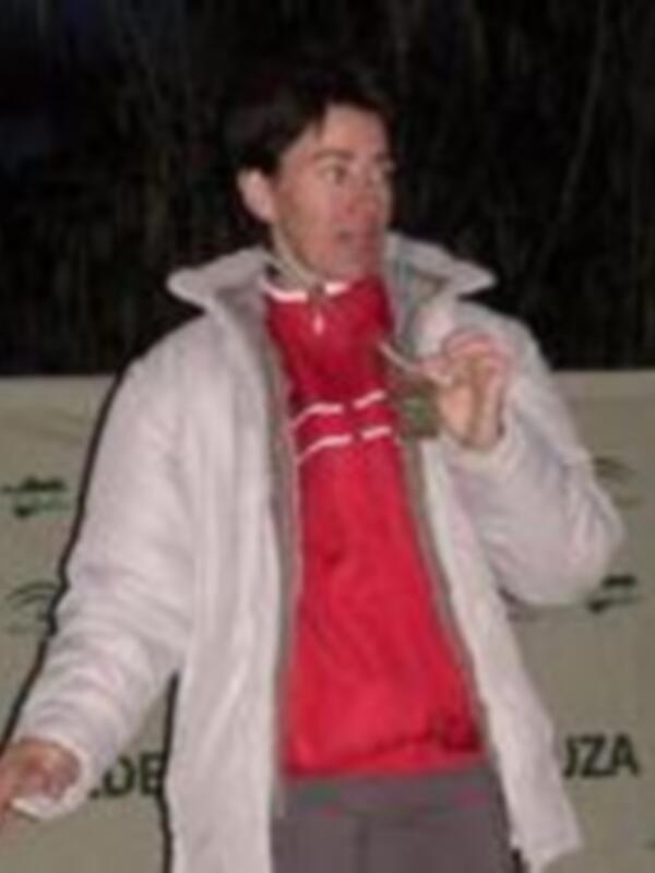 Un hombre con una chaqueta blanca y un suéter rojo está en la nieve, posando con una expresión de alegría.