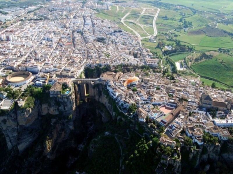Vista aérea de la ciudad de Ronda, España, con su famosa puente colgante y las montañas al fondo.