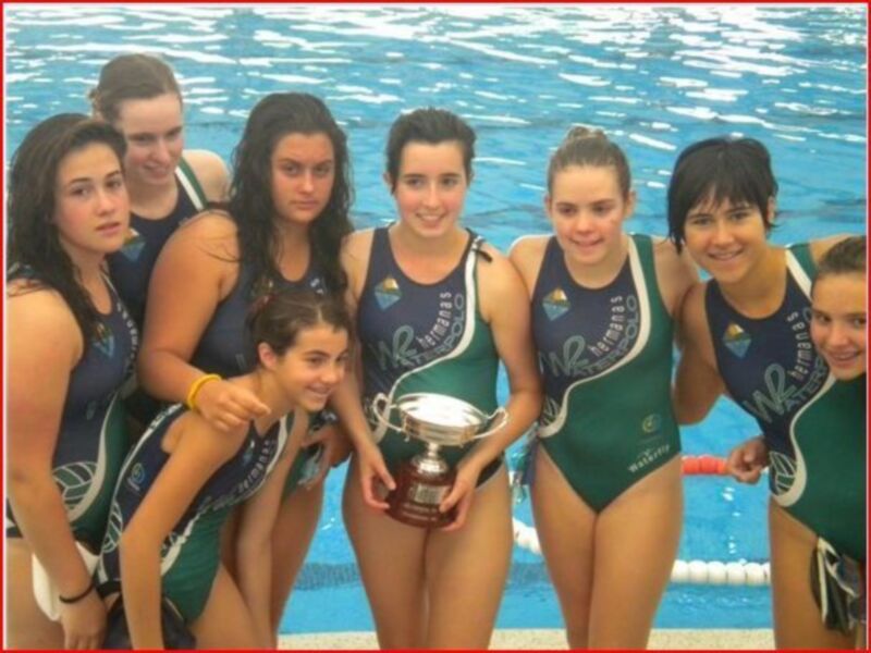 Una joven equipo femenino de natación posa con una copa en la piscina.