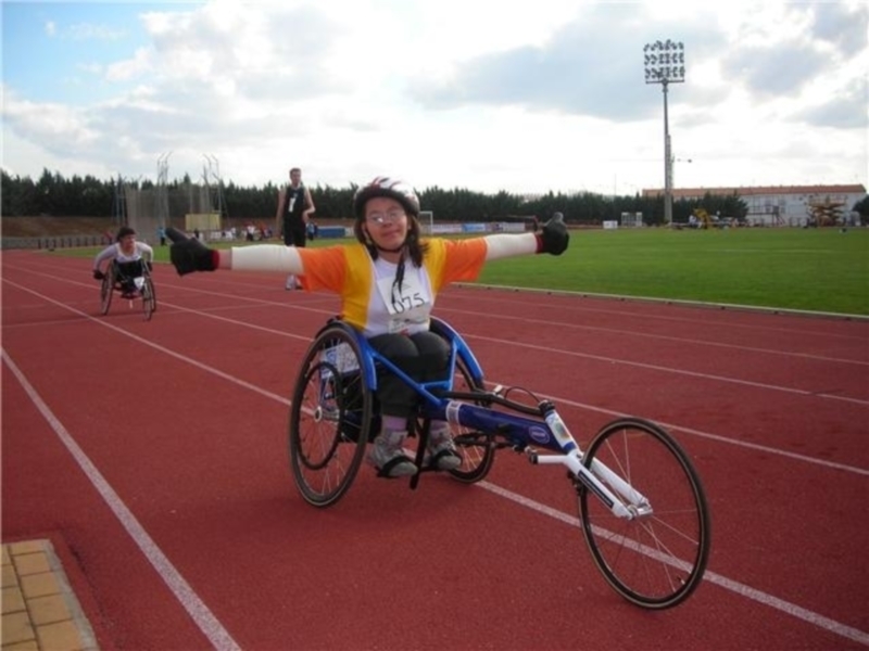 Atleta en silla de ruedas celebrando una victoria en la pista de atletismo.