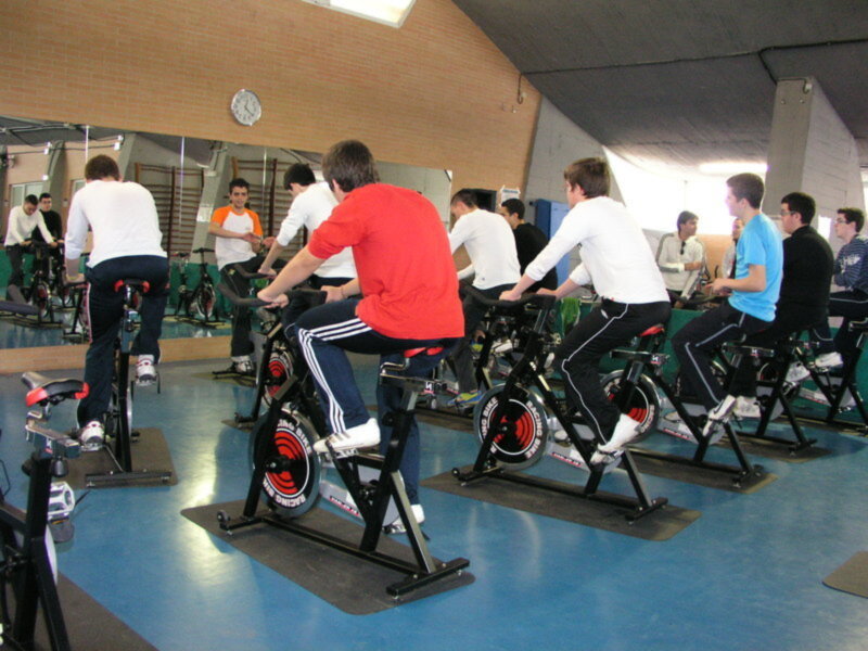Grupo de personas realizando una clase de ciclismo en bicicletas estáticas en un gimnasio.