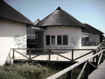 Casa con techo de paja y ventana con grafitis, vista desde un puente de madera.