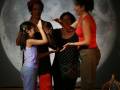 Una escena teatral con cuatro personas en un fondo de luna. Una niña y una mujer están interactuando, mientras que dos mujeres más observan la escena. La imagen sugiere una representación teatral o un espectáculo en vivo.