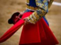 Un torero en traje tradicional sostiene un capote rojo, preparándose para la pelea.