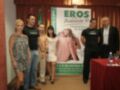 Una imagen muestra a cinco personas posando frente a un cartel promocional del EROS Andalucía 10, evento erótico. La escena está ambientada en un entorno formal con una mesa roja y un cartel informativo.