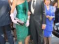 Una mujer viste un vestido verde con un tocado rojo y una señora en azul con un vestido de gala. Un hombre en traje negro con corbata y una mujer en azul con vestido de gala. Todos están en un entorno urbano con edificios y gente a su alrededor.