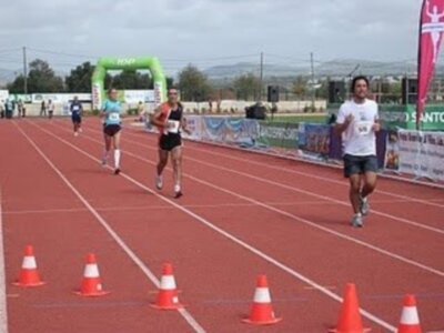 Atletas corriendo en una competencia de atletismo en una pista de atletismo con conos de marcación y banderas de patrocinio.