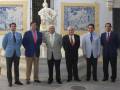 Un grupo de hombres en trajes posa frente a un monumento con azulejos decorativos.