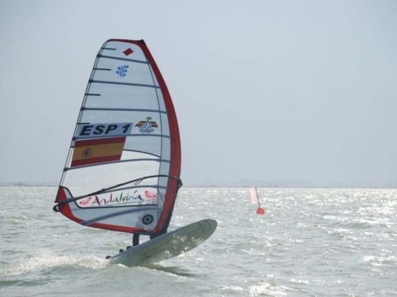 Vela de windsurf con la bandera española y la palabra 'Andalucía' en el mar tranquilo.