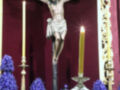 Cristo crucificado en un altar con velas y flores moradas.