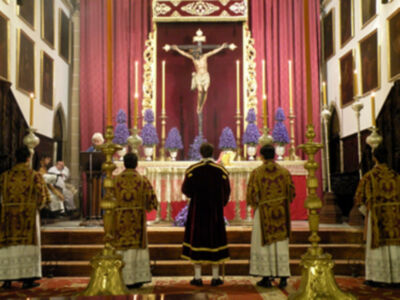 Eucaristía en una iglesia con sacerdotes en trajes ornamentales y un altar con cruces y velas.