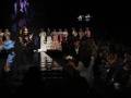 Desfile de moda flamenca con modelos en pasarela y público en el fondo.