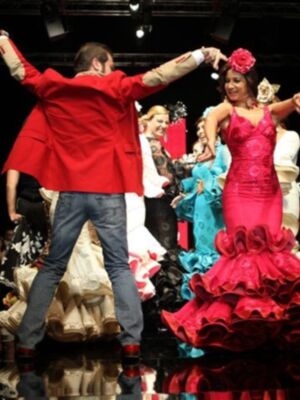 Desfile de moda flamenca con modelos en trajes coloridos y elegantes en un escenario iluminado.