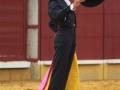 Un torero en traje tradicional sostiene un sombrero negro, preparándose para la corrida de toros en una plaza de toros.