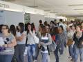 Estudiantes esperando en una fila dentro de un edificio, con carteles y globos decorativos.