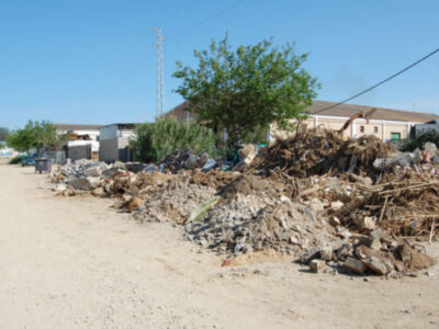Pila de escombros y basura en un área rural, con edificios y árboles al fondo.