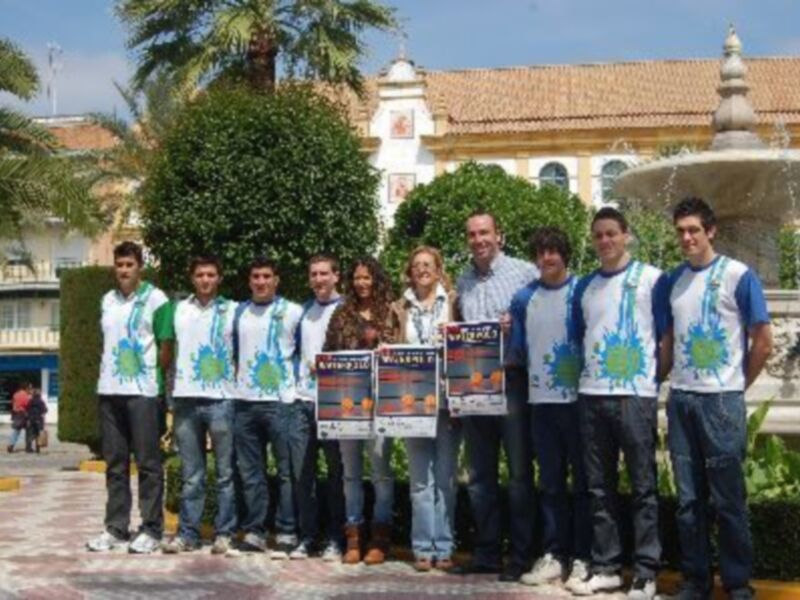 Equipo de jóvenes voluntarios posando con carteles en un parque frente a una fuente y un edificio colonial.