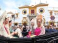 Fotografía de una celebración en Sevilla, España. Personas vestidas con trajes tradicionales y un edificio histórico al fondo.
