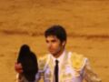 Un torero en traje de luces sostiene un sombrero negro en un ruedo de arena.
