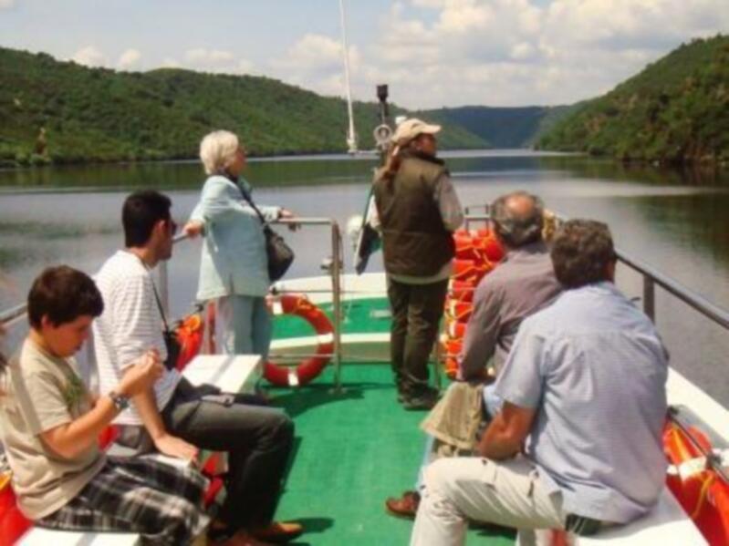 Pasajeros disfrutando de un paseo en barco por el río, con paisajes montañosos alrededor.