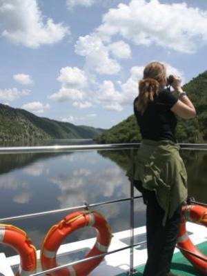 Una mujer toma una foto desde un barco, con el lago y montañas al fondo.