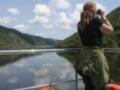Una mujer toma una foto desde un barco, con el lago y montañas al fondo.
