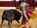 Un torero lucha con un toro en una plaza de toros. El torero usa una capa colorida y una chaqueta dorada, mientras el toro está en el medio de la arena.