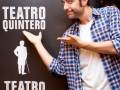 Un hombre con una camisa a cuadros y jeans apuntando hacia un póster de Teatro Quintero.