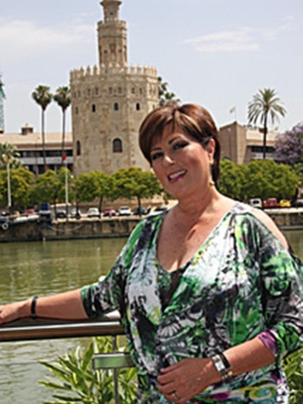 Una mujer con un vestido verde y negro posa frente a la Torre del Oro en Sevilla, España.