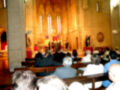 Interior de una iglesia con gente sentada en bancos, vitrales y un altar central.