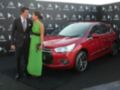 Un hombre y una mujer posan frente a un Citroën DS3 rojo en un evento de presentación. El hombre lleva traje negro y corbata, mientras que la mujer está vestida con un vestido verde largo. El fondo es una pared de logotipos de Citroën, indicando que se trata de un lanzamiento o evento relacionado con esta marca automotriz.