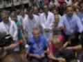 Un hombre en un camiseta azul es entrevistado por varios periodistas con micrófonos. Algunos de ellos llevan auriculares y están en una zona con varios médicos y enfermeras. La escena parece ser en un hospital o centro médico, con una multitud de personas alrededor.